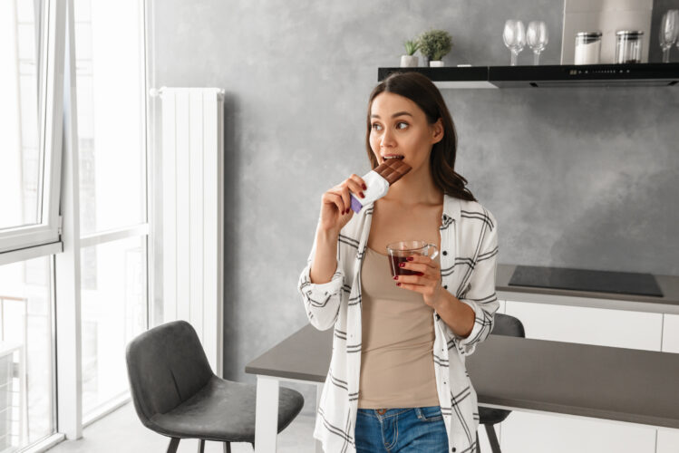 Photo of young pretty woman in casual wear eating chocolate and