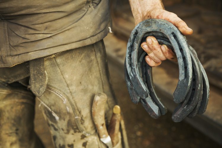 A farrier holding a handful of metal horseshoes.