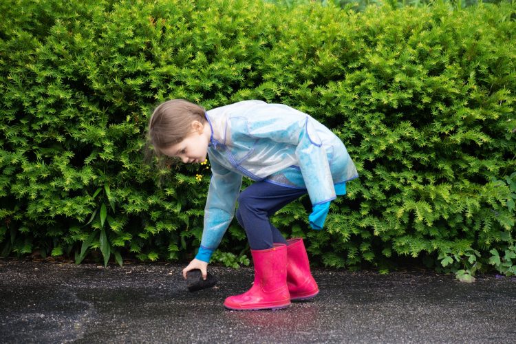 A young girl child stooping over to pick something up outdoors on a rainy day wearing her raincoat