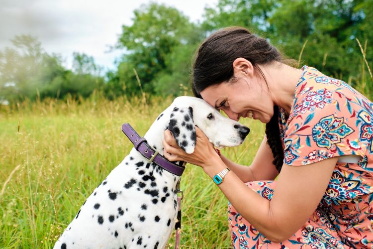 Happy young adult woman looking at her Dalmatian dog and being forehead to forehead in nature