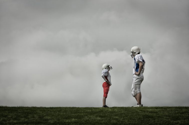 Two football players facing each other, one very tall and one shorter person looking up.