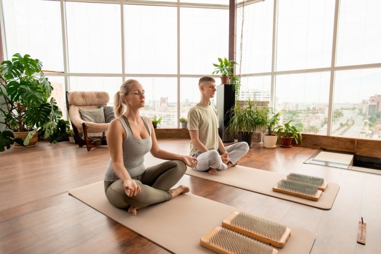 Young serene couple in sportswear sitting in pose of lotus and meditating