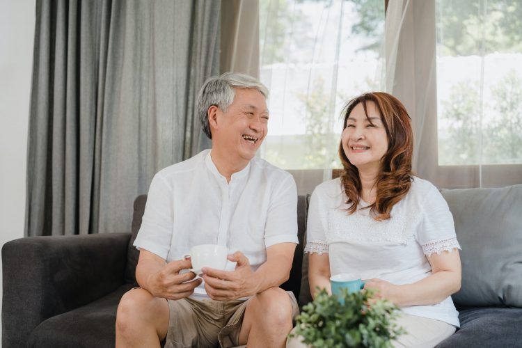 Asian senior couple relax at home. Husband and wife smile talking and drinking coffee