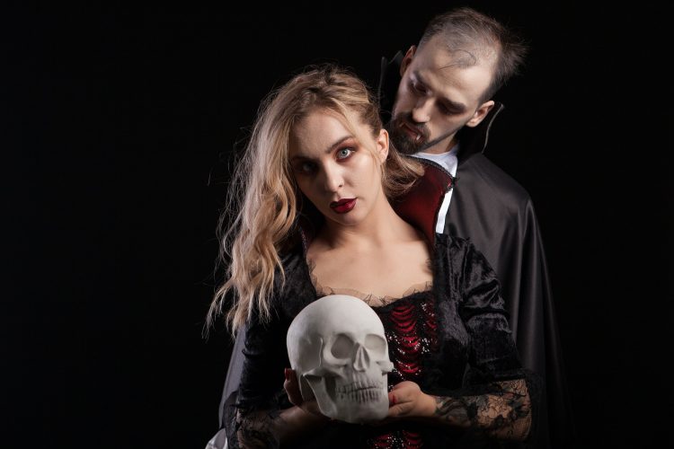 Portrait of young man dressed up like Dracula looking at the neck of his vampire woman