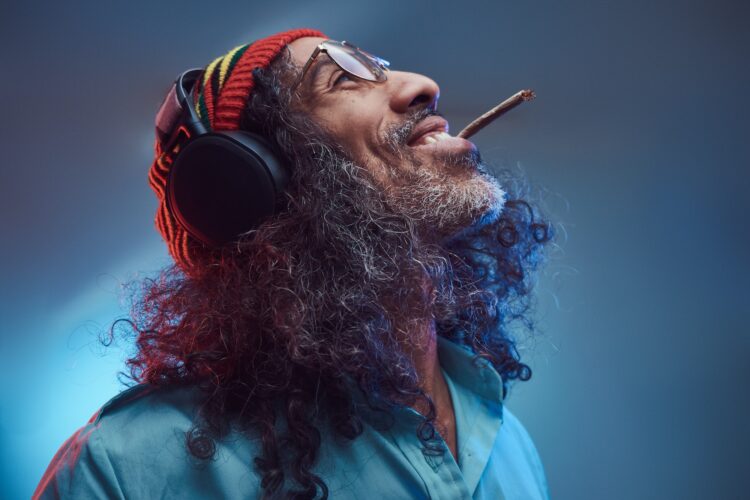Studio portrait of African Rastafarian male enjoys music in headphones and smoking weed.
