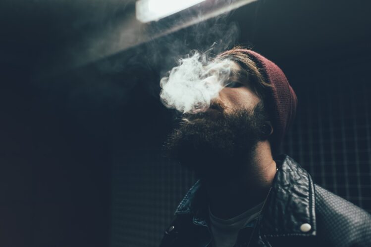 Young male hipster in knit hat smoking at night