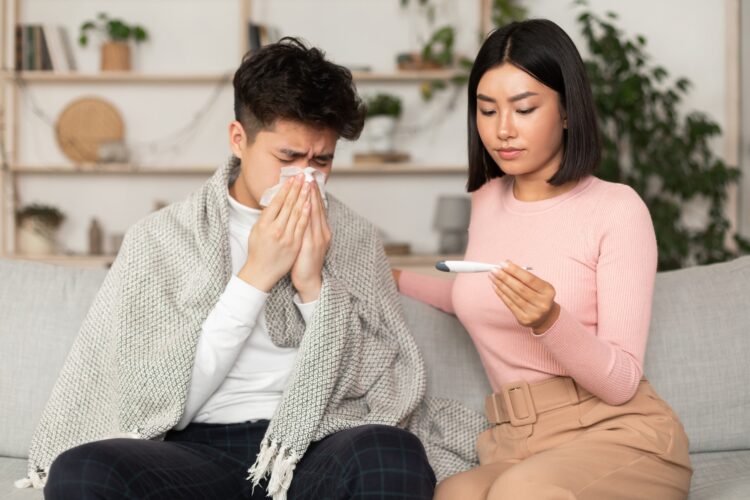 Girlfriend Treating Sick Boyfriend Giving Medicine Sitting On Couch Indoor