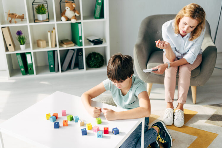high angle view of irritated kid with dyslexia playing building blocks and child psychologist