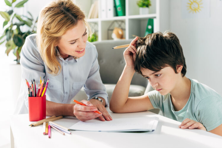 kid with dyslexia and smiling child psychologist sitting at table and holding pencils