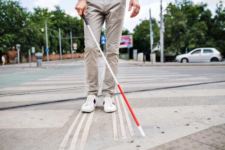 Midsection of young blind man with white cane walking across the street in city