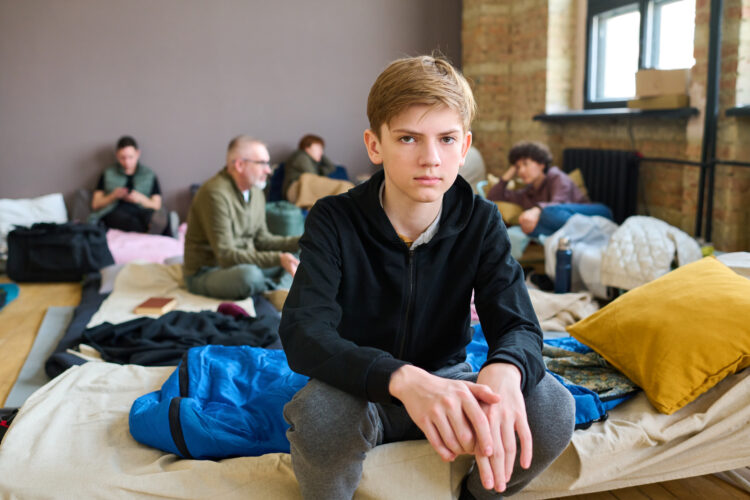Serious boy in casualwear sitting on couchette prepared for homeless people