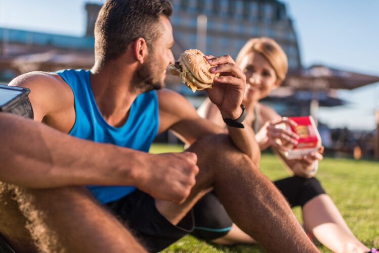 athletic sportswoman and sportsman eating junk food